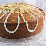 A round Classic Lemon Almond Pound Cake with lemon drizzle and toasted almonds on top, presented on a plate.