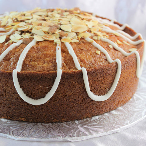 A round Classic Lemon Almond Pound Cake with lemon drizzle and toasted almonds on top, presented on a plate.