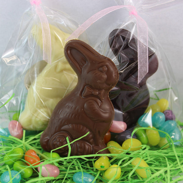 A solid chocolate Easter Bunny with Jelly Belly's, packaged in a clear bag with a pink ribbon, sitting on green grass with colorful Easter eggs around it.