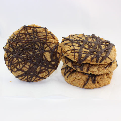 An image showing 4 flourless peanut butter cookies with chocolate drizzle. The dairy free cookies are stacked on a white background.
