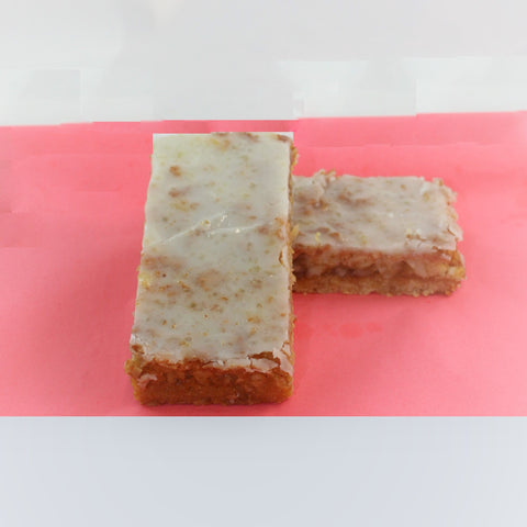 2 pieces of no gluten added lemon dream bar on a pink and white background, with a thick lemon glaze on top.