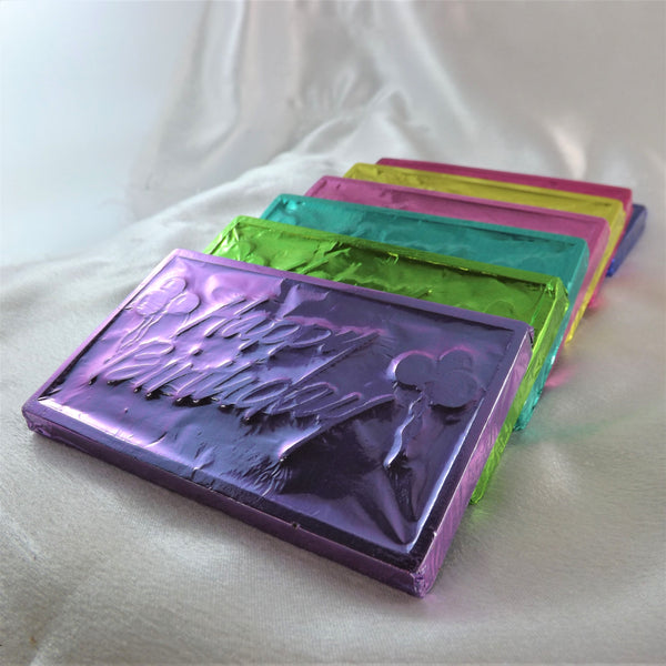 A collection of solid no sugar added birthday chocolate bars wrapped in colorful foil, displayed on a soft surface.