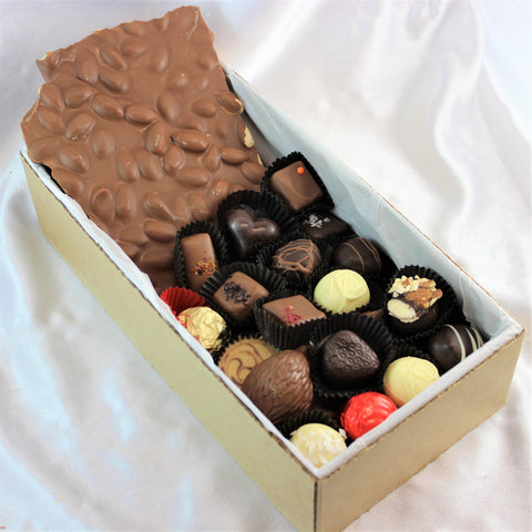 A box of perfectly imperfect 'Oops' Chocolates & Bark with a variety of shapes and sizes, some with a glossy finish and others with a textured design. The chocolates are displayed in a box on a white surface.