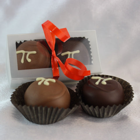 A photo of 2 Hand Dipped Pumpkin Pi Chocolate Truffles on a white background, with a boxed version behind, presented in a clear packaging with a red ribbon.