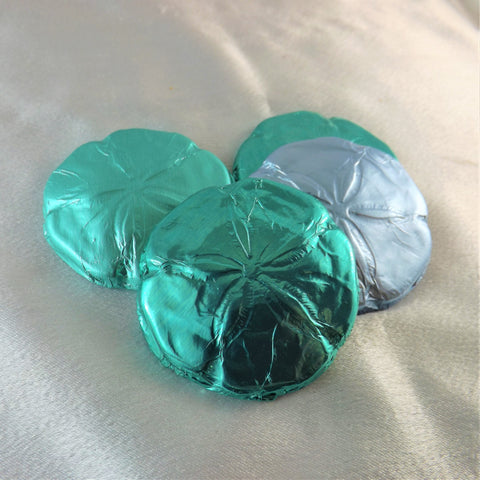 Wrappers resembling solid chocolate sand dollars, in silvery greens, on a silky beige surface.