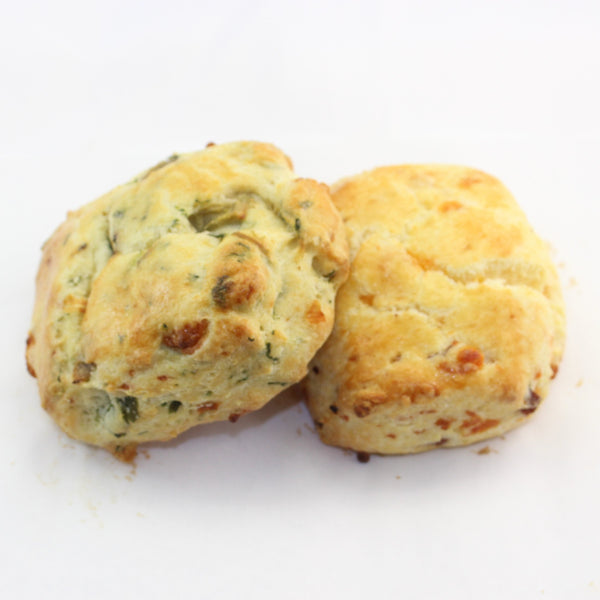 Two golden brown fresh baked savoury scones with herbs and cheese visible within.