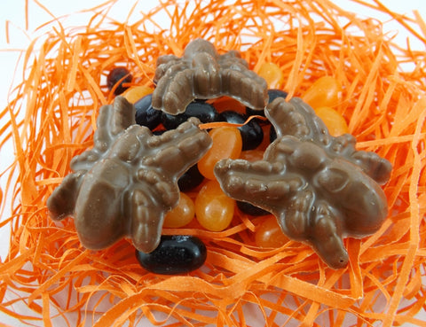 A picture showing the contents of a Spider & Candy Halloween Treat Bag, with 3 chocolate spiders on top of a pile of orange and black jelly beans, on a bed of orange shred.