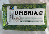 A dark grean bag with gold highlights filled with coffee beans, labeled 'fairtrade' and USDA organic certified, medium roast by Caffe Umbria.