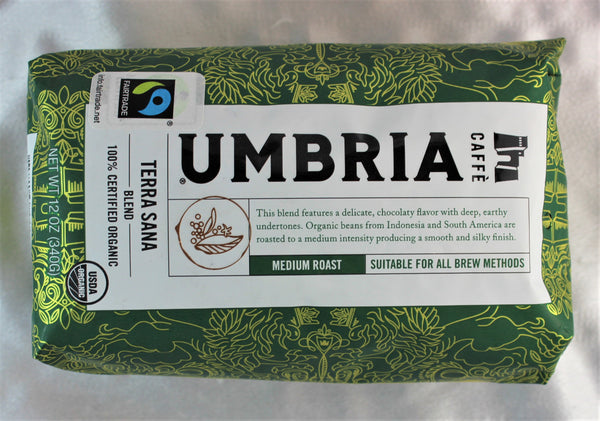 A dark grean bag with gold highlights filled with coffee beans, labeled 'fairtrade' and USDA organic certified, medium roast by Caffe Umbria.