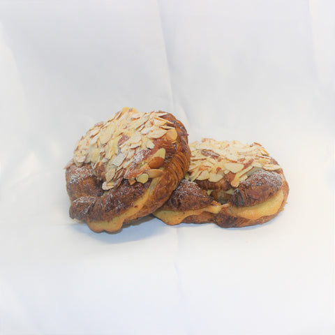 Two fresh baked almond croissants with flaky crust, frangipane and topped with sliced almonds and confectioners' sugar, on a white background.