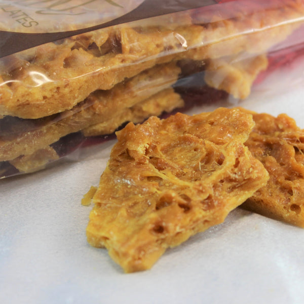Packaged and loose pieces of artisan brittle with freshly roasted nuts, showing the texture and color of the confection.