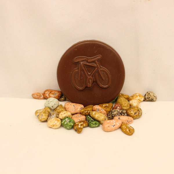 A solid chocolate bicycle coin with chocolate candies made to look like rocks, on a white background.