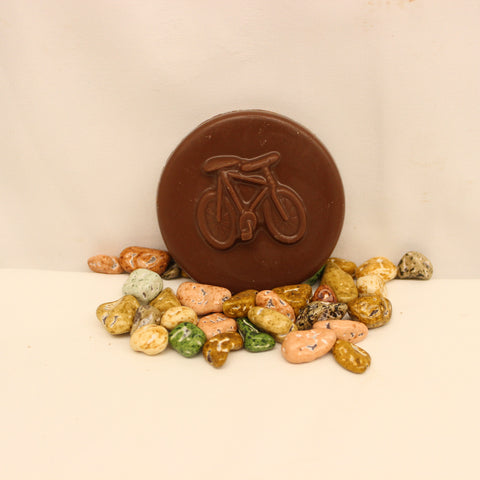 A solid chocolate bicycle coin with chocolate candies made to look like rocks, on a white background.