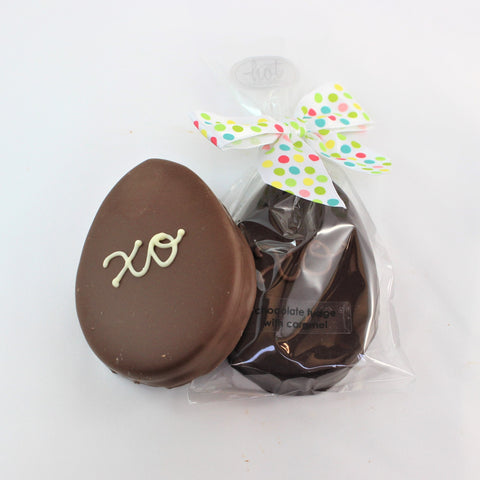 A caramel fudge Easter egg with caramel and fudge layers, wrapped in a clear plastic packaging with a green and white polka-dot ribbon on top.