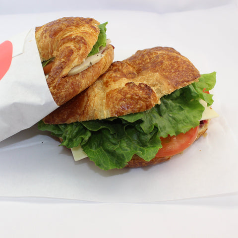 2 artisan chicken croissant sandwiches on bakery paper and a white background.
