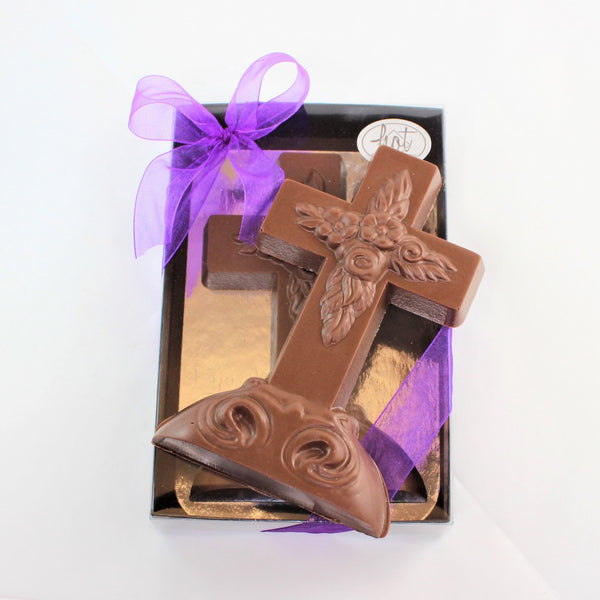 A beautiful solid chocolate Easter Cross, embellished with flowers, on top of a packaged version with a purple bow. 