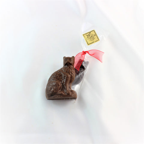 A solid artisan chocolate cat in milk chocolate with a packaged dark chocolate version behind, with a red ribbon on a white background.