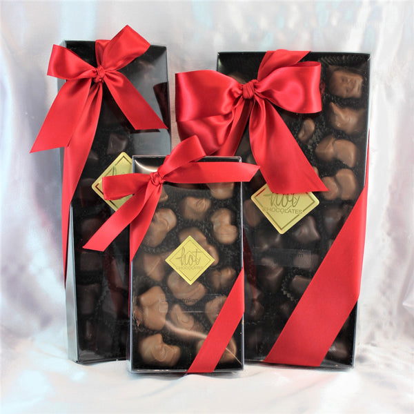 Three rectangular gift boxes of chocolate dipped stem ginger, each adorned with a red ribbon bow and set against a draped white background.