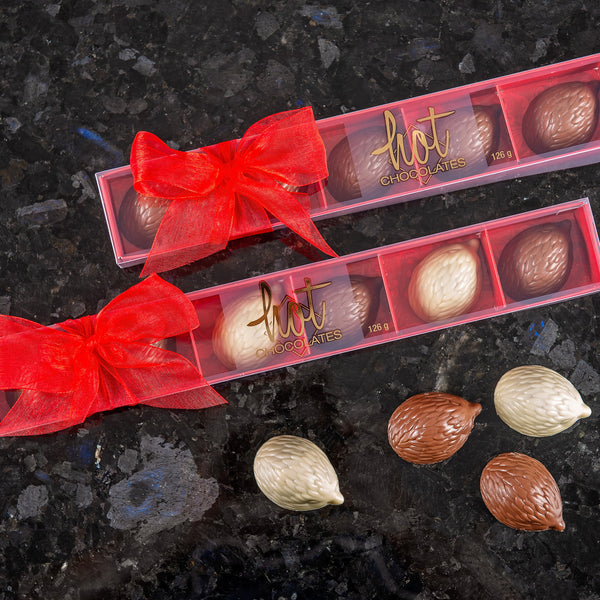 A selection of chocolate hedgehogs with a hazelnut gianduja centre, presented in milk and white chocolate varieties, arranged in a clear packaging with red bows.
