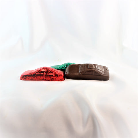 Three solid Colombian chocolate race cars. 2 wrapped in bright foil and 1 unwrapped, presented on a white surface.