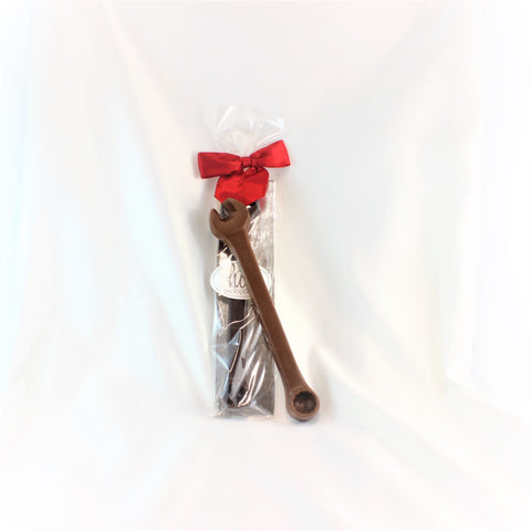 A solid chocolate mechanics wrench in milk chocolate, sitting on top of a 2nd one package with a red bow on a white background.