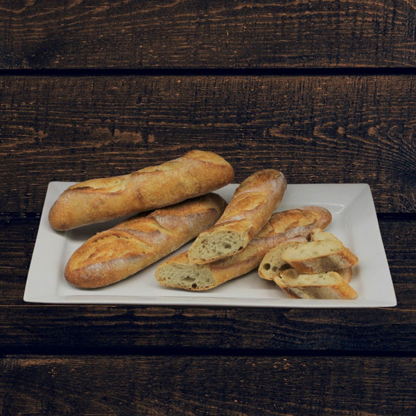 A white plate filled with classic French Baguette, sliced and whole on a rustic wood background.