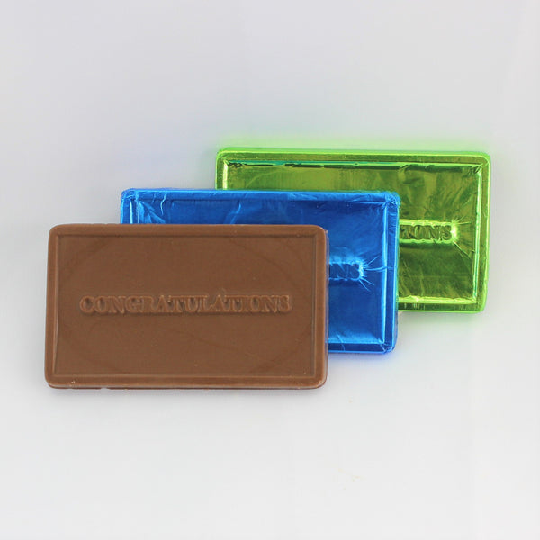 Three rectangular solid congratulations chocolate bars in blue, and green wrappers with the words 'CONGRATULATIONS' written on them, with a single milk chocolate example in front.