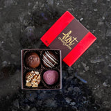 An example box from the Build your own custom truffle box catalogue, showing 4 assorted chocolate truffles in a red and brown box.