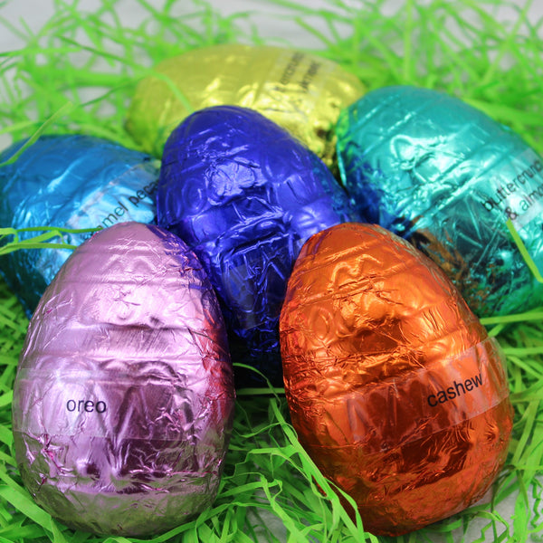 A collection of colorful filled 1/2 Easter eggs wrapped in metallic foil, displayed on green grass.