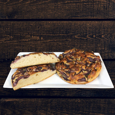 A photo of herb & cheese focaccia bread on a white plate, with herbs and cheese toppings, presented on a wooden table.