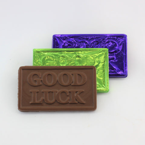 A solid Good Luck chocolate bar with brightly colored foil in green and purple, and a milk chocolate bar with the text 'Good Luck' embossed on it.