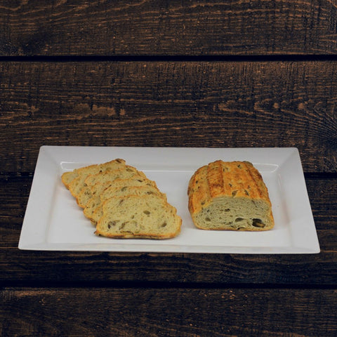 A loaf of Mediterranean olive & thyme bread with slices cut, on a white plate, against a wooden background
