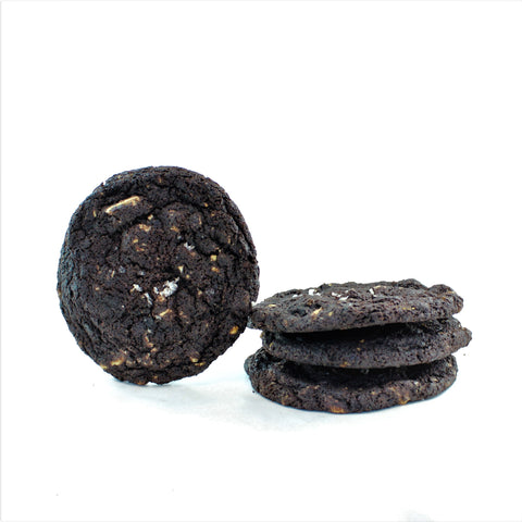 A stack of sweet & salty double chocolate cookies with visible white chocolate chunks and sea salt flakes, with a single cookie leaning against the stack on a white background.