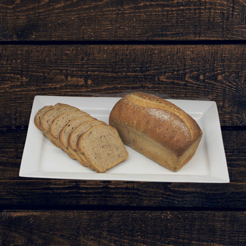 A loaf of ancient grain spelt bread, partially sliced, on a white plate against a wooden background.