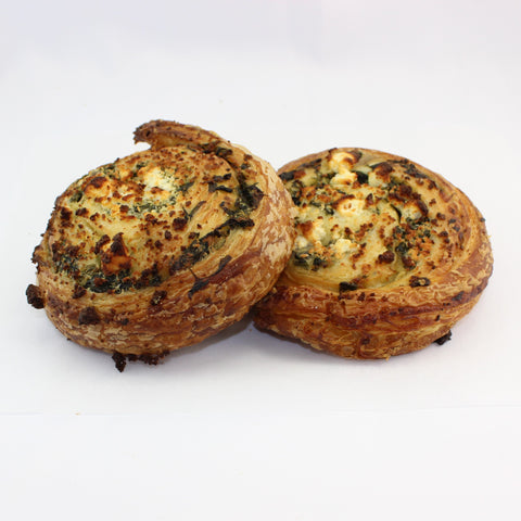 Two savoury spinach and feta croissant pinwheels on a white background.