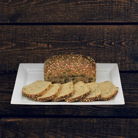 Sliced loaf of honey oat whole wheat bread with sunflower seeds on a white plate, with the loaf partially sliced to show the soft interior.