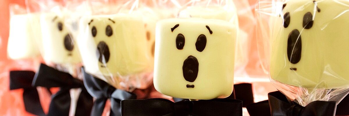 Halloween chocolate marshmallow Ghost Pops with scared faces and black bows.