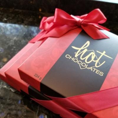 A red and brown chocolate box with a gold Hot Chocolates logo and a red bow.