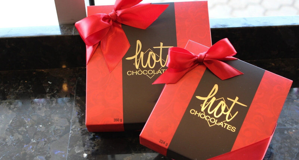 A stack of Hot Chocolates truffle boxes in green and pastel finsihed with a yellow bow.